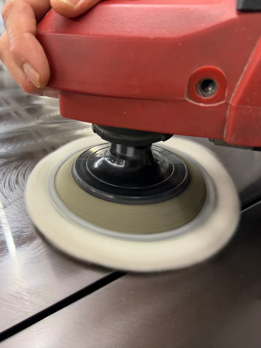 Rotationspoliermaschine mit Lammfellpad bei der Lackpolitur auf dunklem Lack