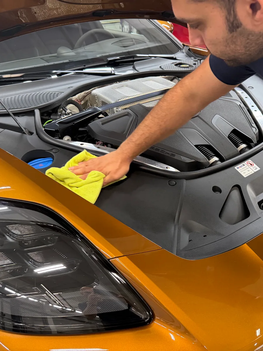 Mitarbeiter reinigt die Abdeckungen im geöffneten Motorraum mit einem Mikrofasertuch