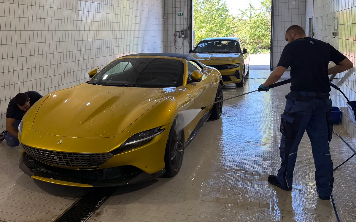 Zwei Mitarbeiter waschen in unserer Waschhalle einen gelben Sportwagen, einer mit dem Hochdruckreiniger, Außenaufbereitung im CarCare Center Leipzig