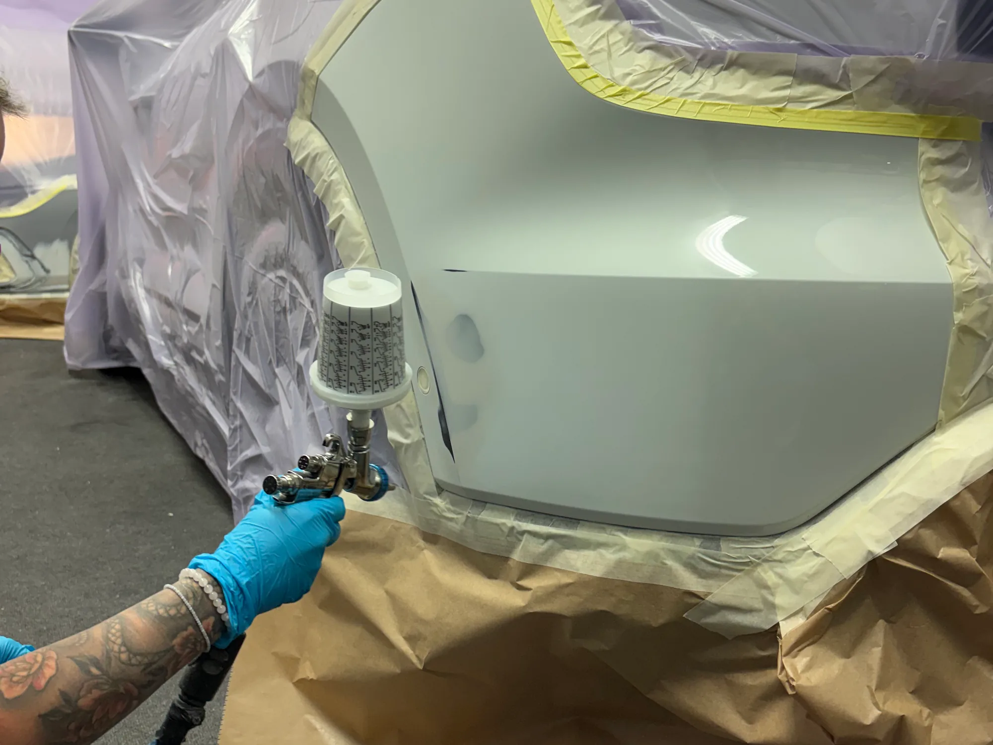 Lackierer trägt mit der Lackierpistole Lack auf einen abgeklebten Stoßfänger auf, Smart Repair im CarCare Center Leipzig